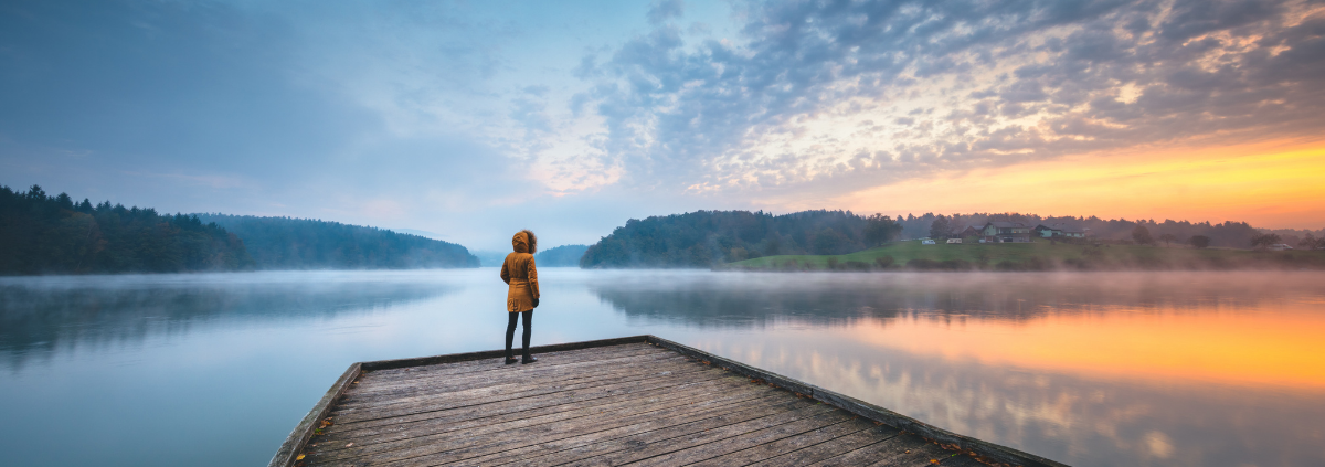 Person standing on a pier staring at the sunset over water