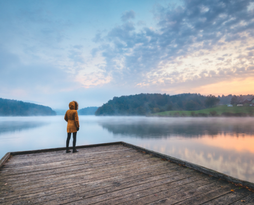 Person standing on a pier staring at the sunset over water