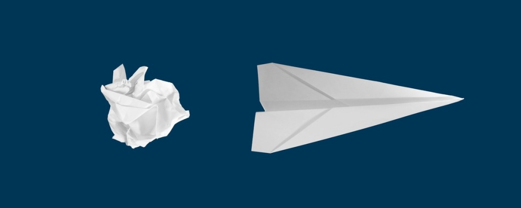 Crumpled paper ball beside a folded white paper airplane on a navy background