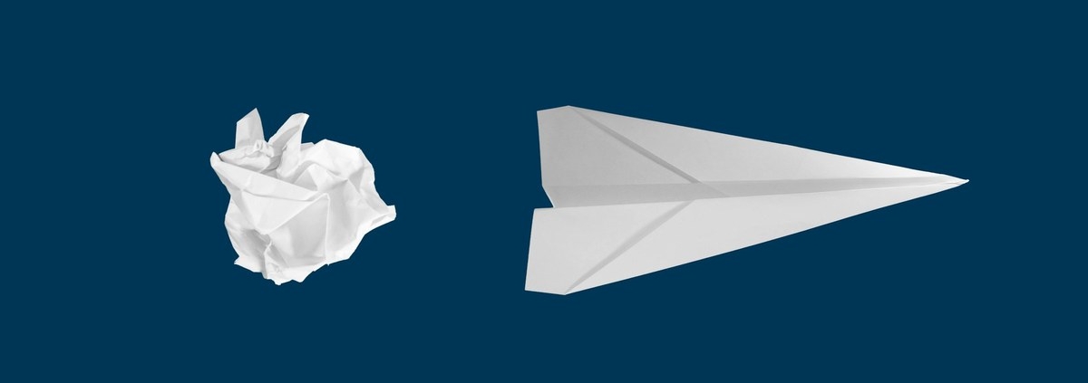 Crumpled paper ball beside a folded white paper airplane on a navy background