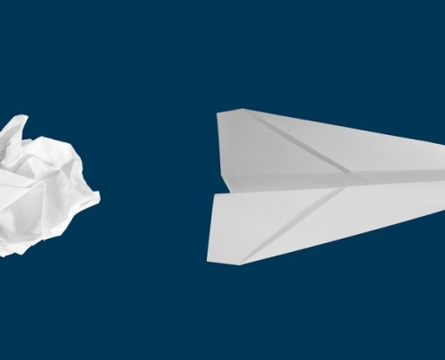Crumpled paper ball beside a folded white paper airplane on a navy background